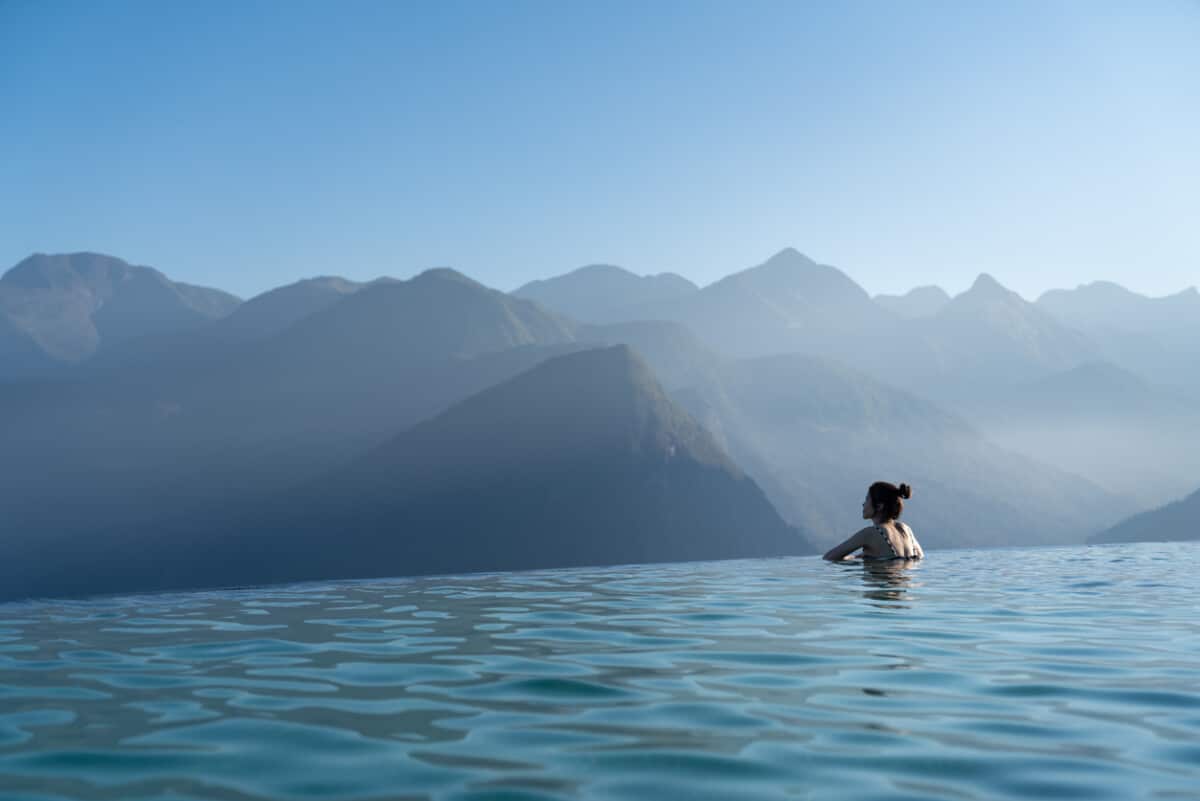 Sexy woman relaxing in infinity swimming pool looking at stunning mountain view at luxurious resort / vacation concept