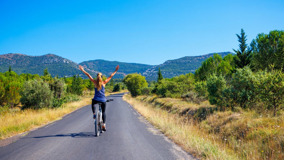 Happy woman with open arms on bike riding on the road- France- travel, sport, active woman concept