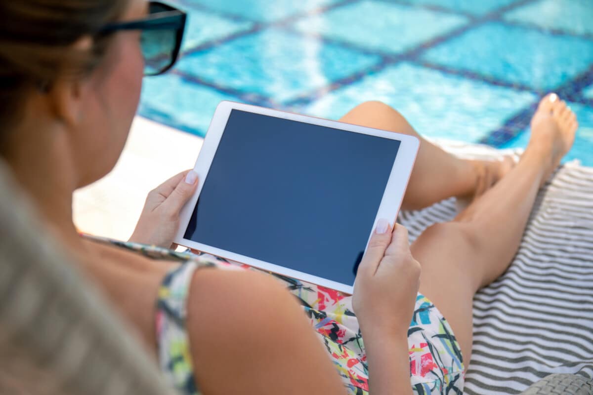 woman hands holds white computer tablet with blue screen near the pool