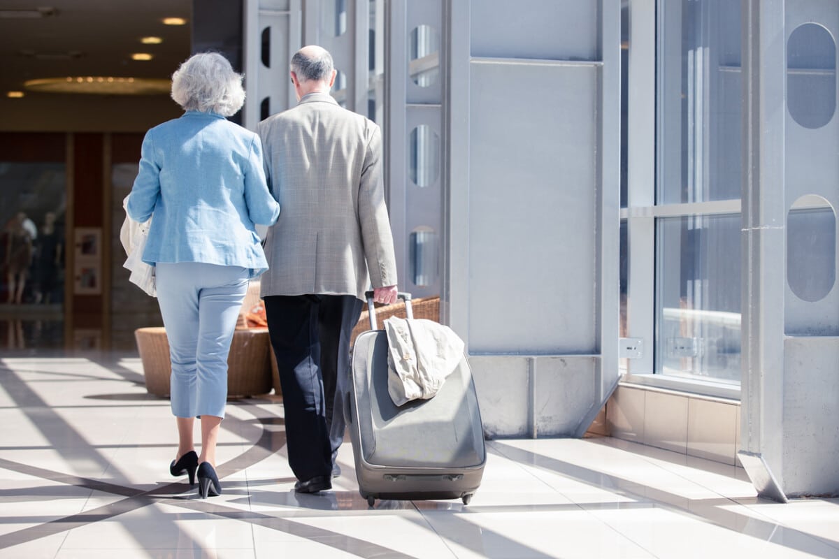 Senior couple in airport walking with suitcase. Holiday travel background.