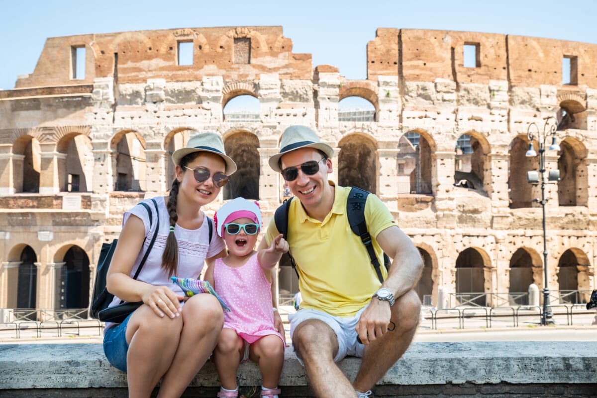 Young Tourist Family Sitting In Front Of Colosseum In Rome, Italy