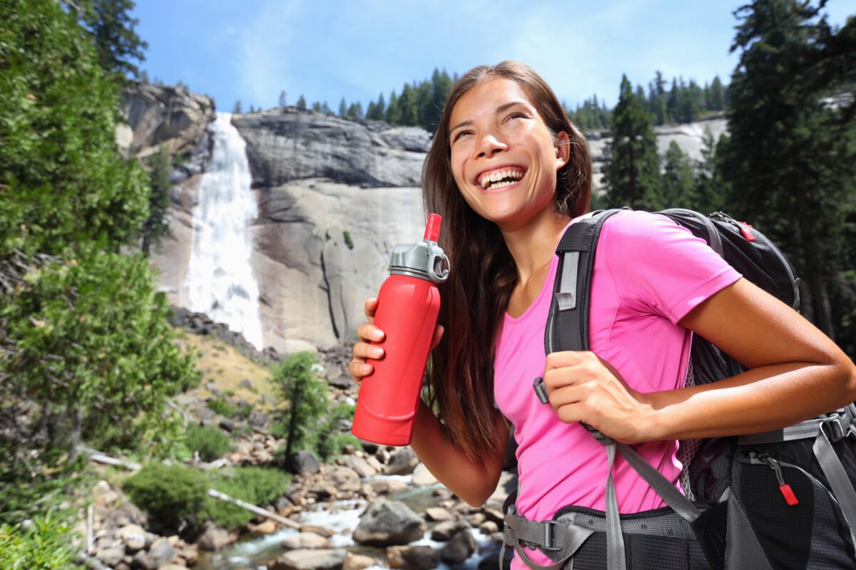 Healthy hiker girl drinking water in nature hike. Beautiful young woman hiking happy with water bottle in front of Vernal Fall, Yosemite National Park, California, USA.