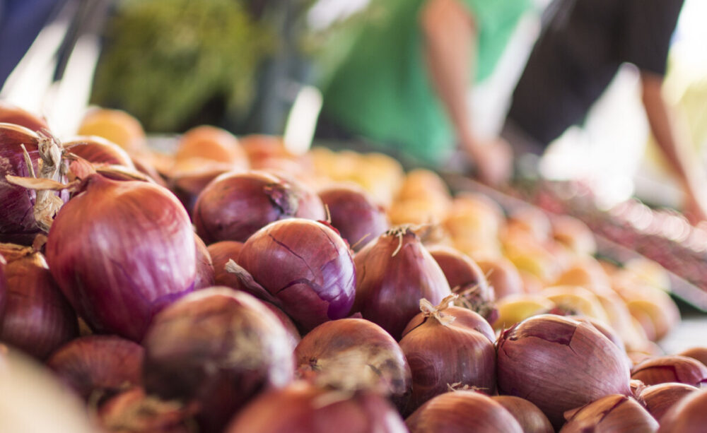Vibrant red onions stacked in a pile near many other vegetable choices at a farmers market in Sacramento, California.